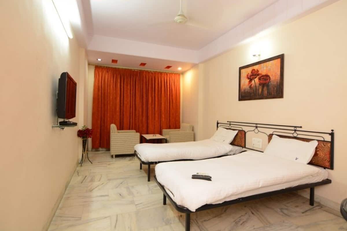 A hotel room with two single beds, a flat-screen TV, a painting, and a large window with curtains.