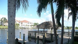 A waterfront dock with a thatched structure, surrounded by palm trees and a body of water. - Beautiful open sunny Condo on waterfront dock with Gulf access in  Cape Coral Fl (Cape Coral)