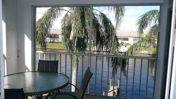 A balcony with a glass table and chairs, overlooking a body of water and palm trees. - Beautiful open sunny Condo on waterfront dock with Gulf access in  Cape Coral Fl (Cape Coral)