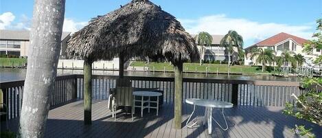 Eine Holzterrasse mit einem Gazebo mit Strohdach, Tischen und Stühlen.