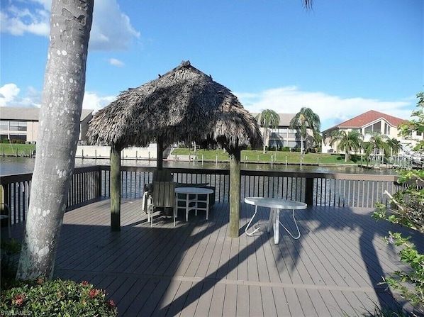 A wooden deck with a thatched-roof gazebo, tables, and chairs.