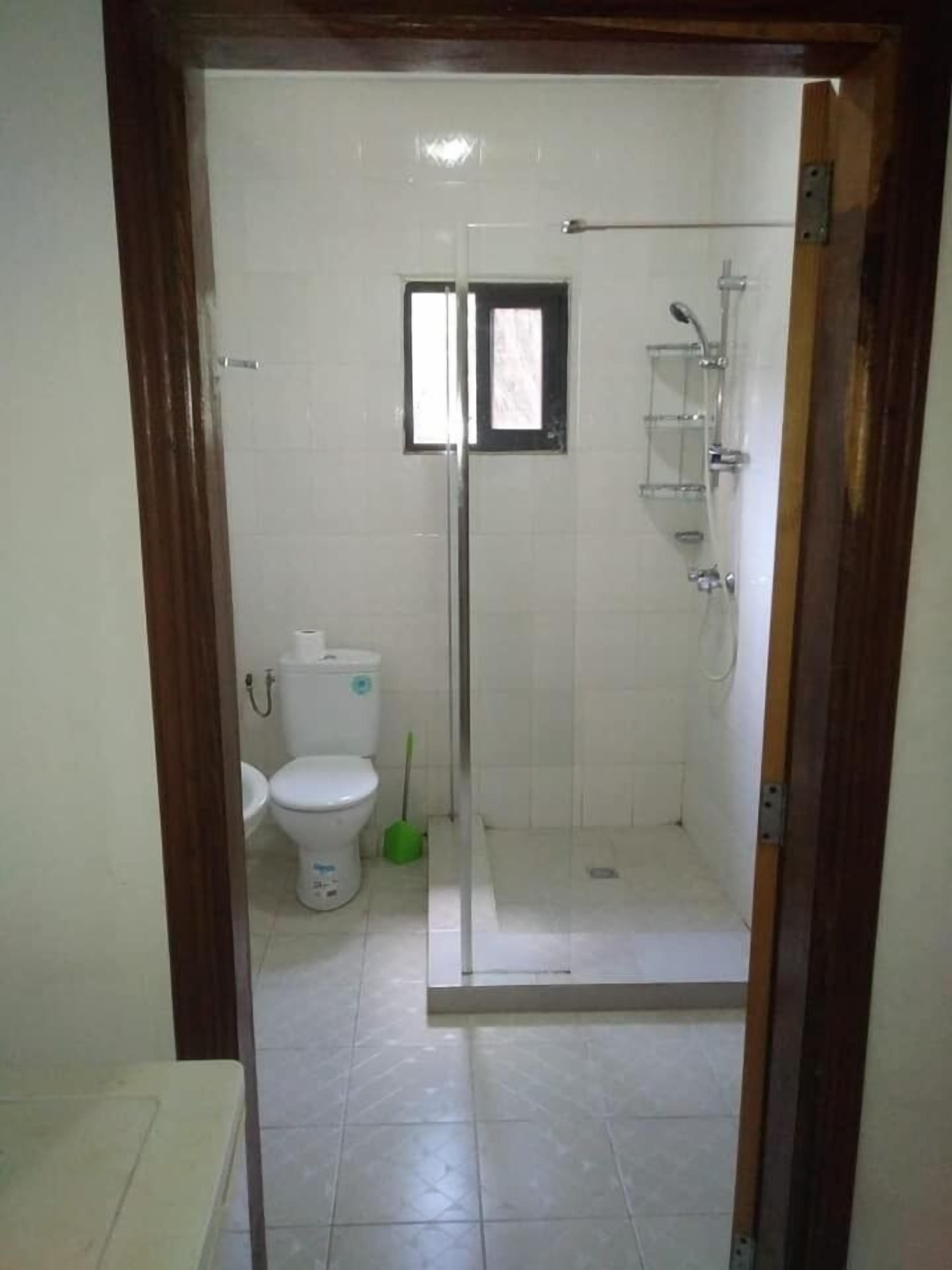 Et badeværelse med glasbrusekabine, toilet og et vindue.