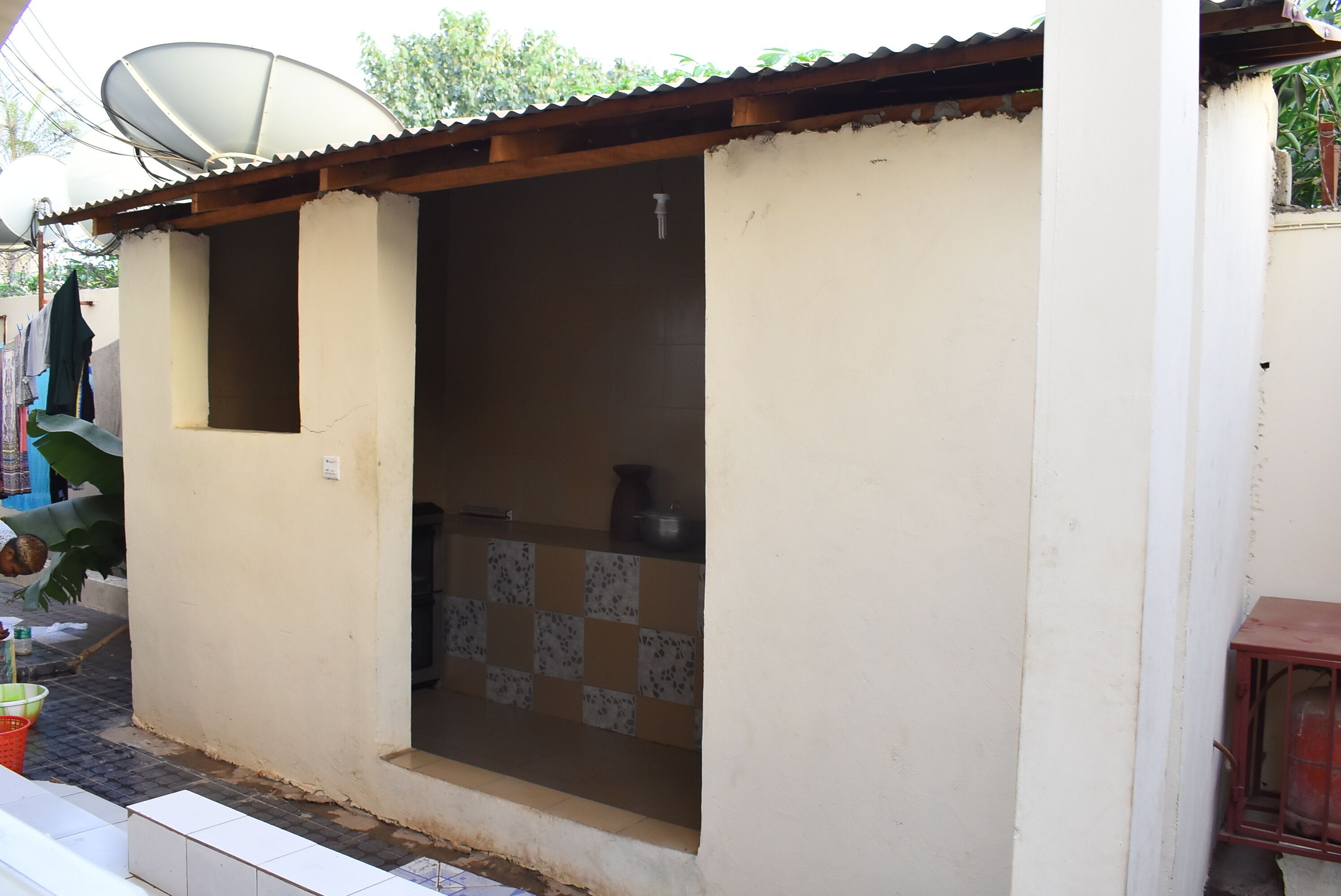 Uma casa pequena, de um único cômodo, com cozinha em ladrilho, antena parabólica e uma pequena janela.