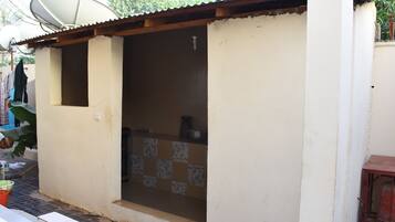 Uma casa pequena, de um único cômodo, com cozinha em ladrilho, antena parabólica e uma pequena janela.