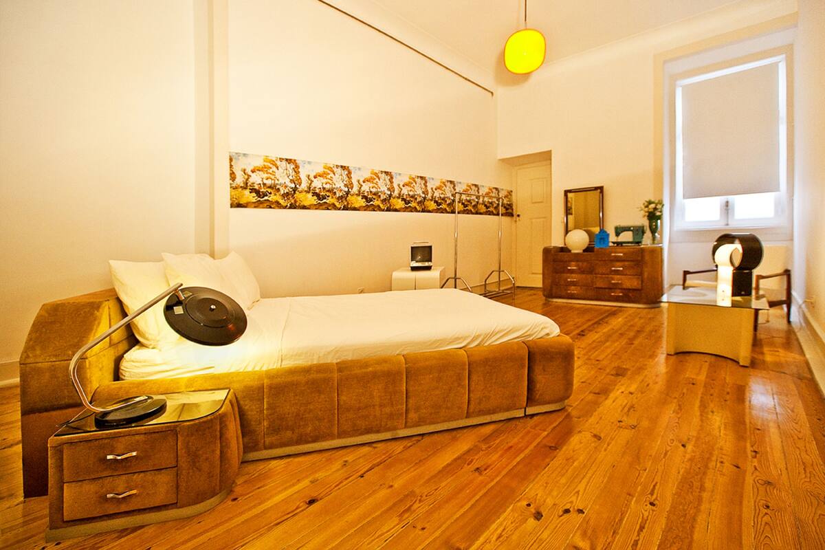 A bedroom with a bed, bedside table, lamp, dresser, and a painting on the wall.
