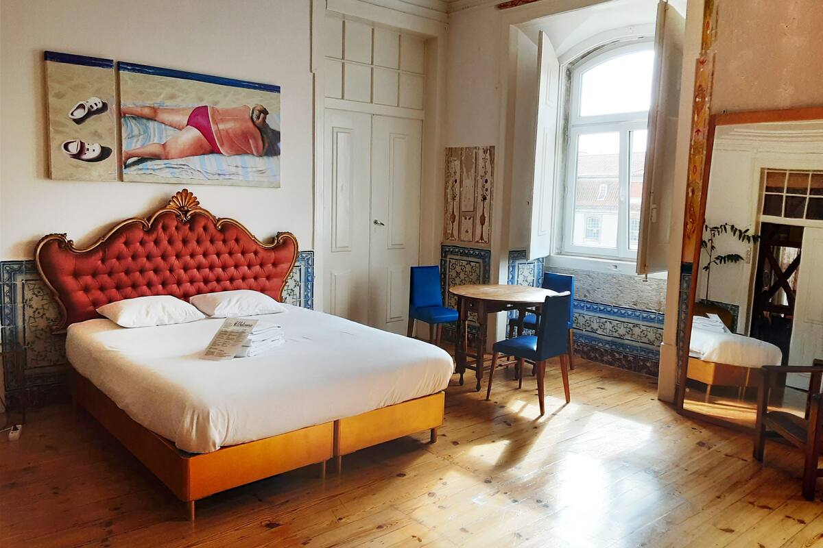 A hotel room with a large bed, a small table, two chairs, and a window with a view.