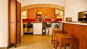 A compact kitchen with a brick arch, a washing machine, a toaster, and wooden stools. - Lisbon Calling (Lisbon)