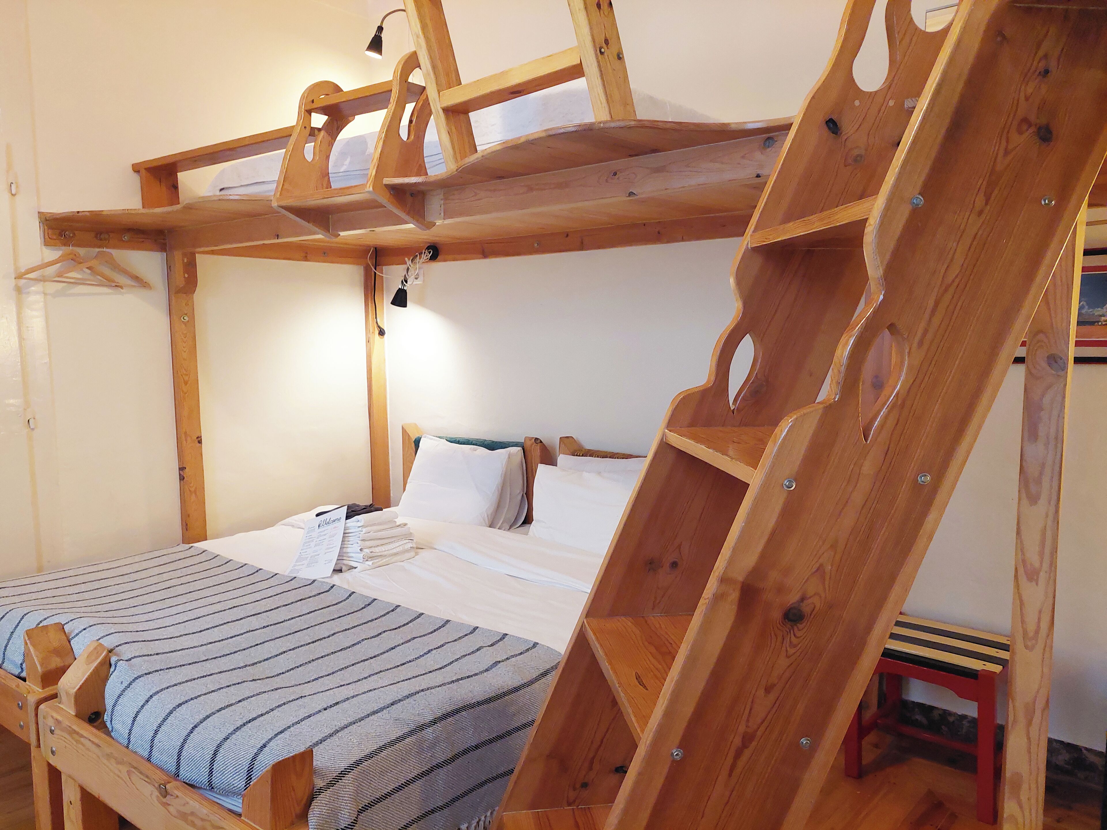 Ein Holzbett mit Etagen, eine Nachttischlampe und ein kleiner roter Hocker.