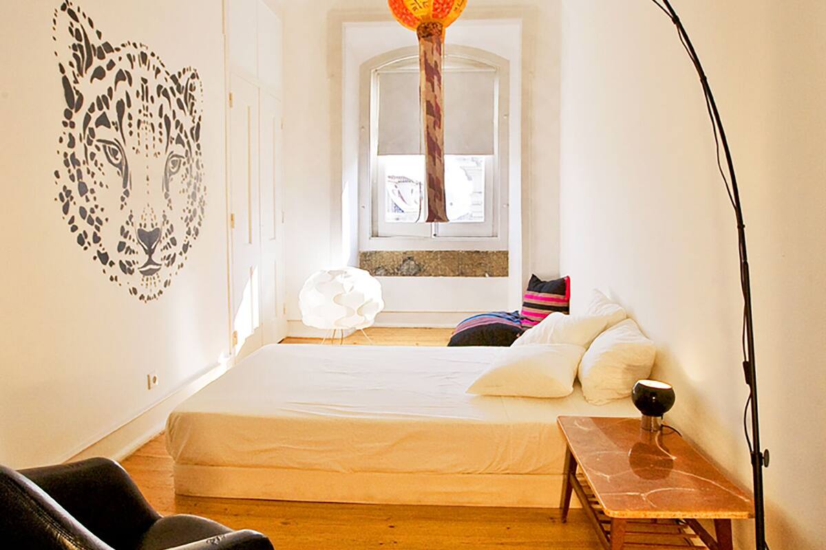 A compact bedroom with a loft bed, a desk, a chair, and a floor lamp.