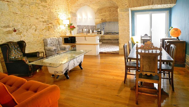 A spacious living area with a stone wall, a dining table with chairs, a sofa, and a kitchen in the background. - Lisbon Calling (Lisbon)