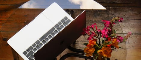 A laptop on a wooden table with a vase of flowers.