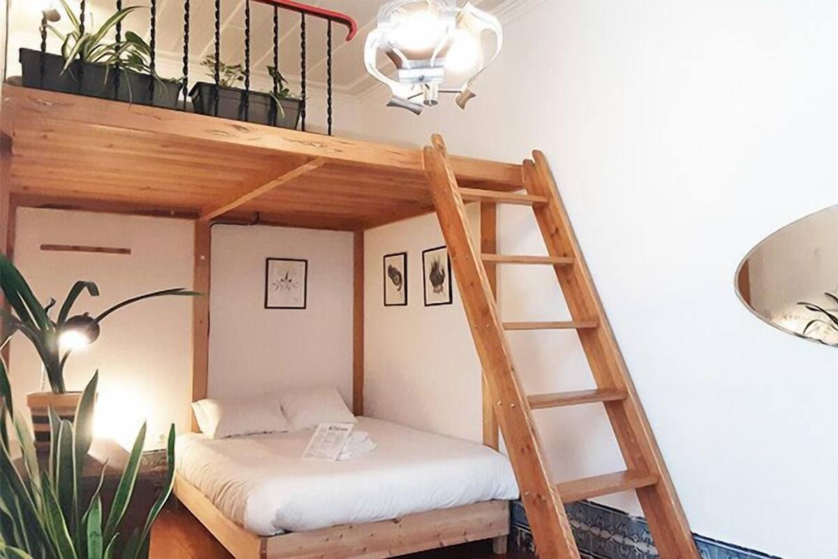 A bunk bed with a wooden ladder, a small balcony with plants, and a ceiling light fixture.