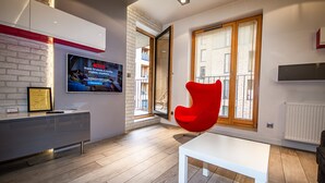 A modern living room with a red chair, a flat-screen TV, and a white table.