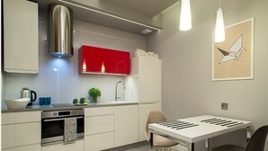 A modern kitchen with stainless steel appliances, a red cabinet, and a dining area with a white table and chairs.