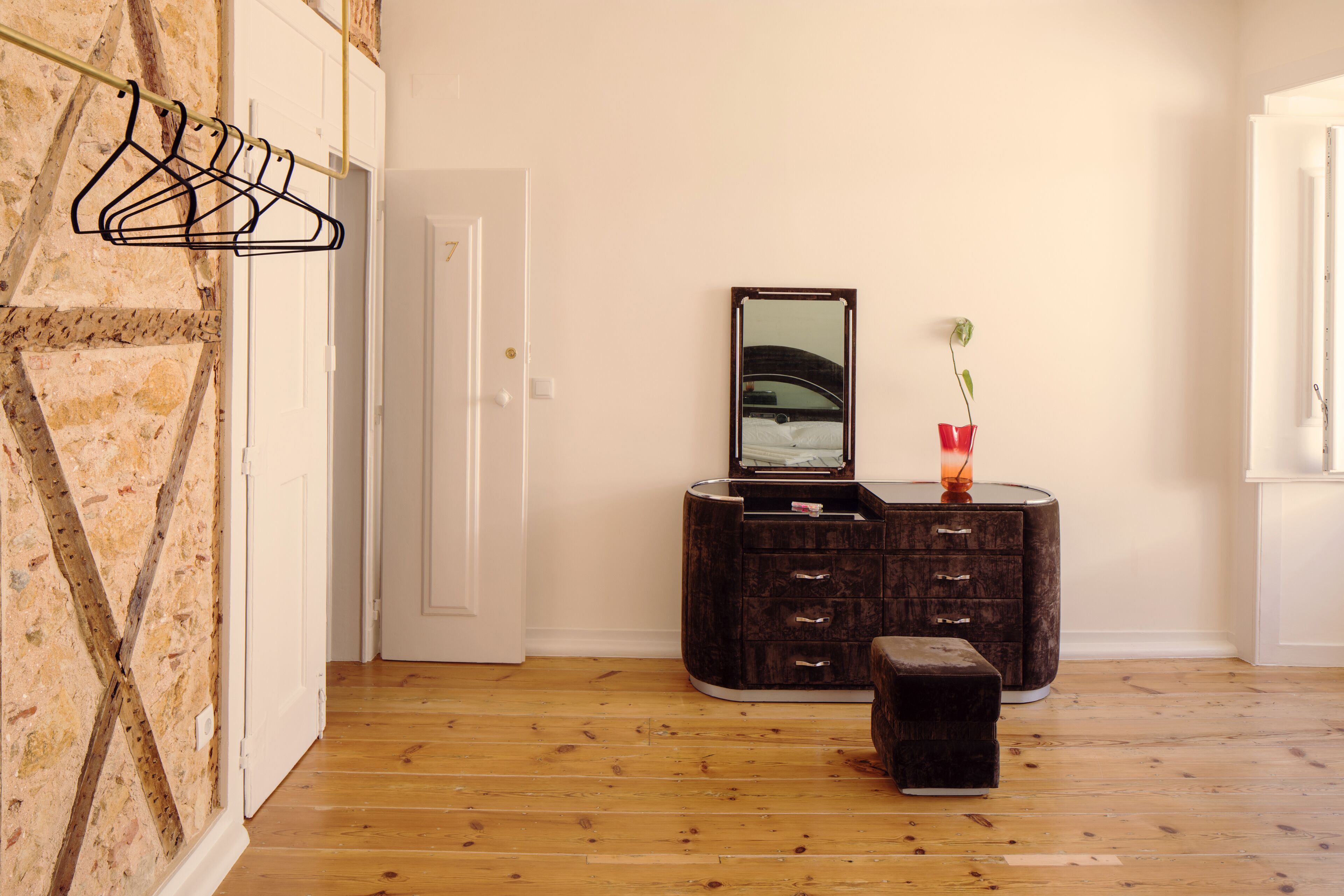 Ein Zimmer mit Holzboden, einer dunklen Holzkommode mit Schubladen, einem Spiegel und einer kleinen Bank.