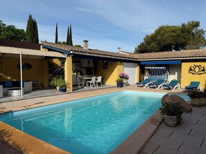 A swimming pool with lounge chairs, a covered patio area, and a yellow building with a lotus symbol.