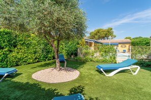 A well-maintained garden with two lounge chairs, a tree, and a building with a blue roof in the background. - Provencal house with all comforts. Pool & air-conditioning, PK pets allowed. (L'Isle-sur-la-Sorgue)