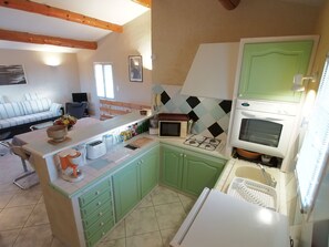 A compact kitchen with a microwave, stove, and refrigerator. There is a dining area with a table and chairs, and a sofa in the background. - Provencal house with all comforts. Pool & air-conditioning, PK pets allowed. (L'Isle-sur-la-Sorgue)