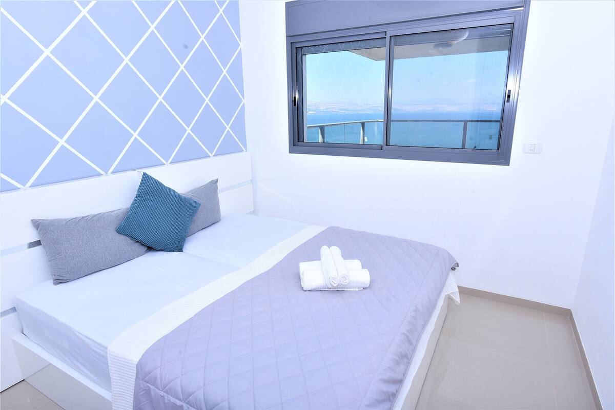 A neatly made bed with a quilted bedspread, a pillow, and a rolled towel.