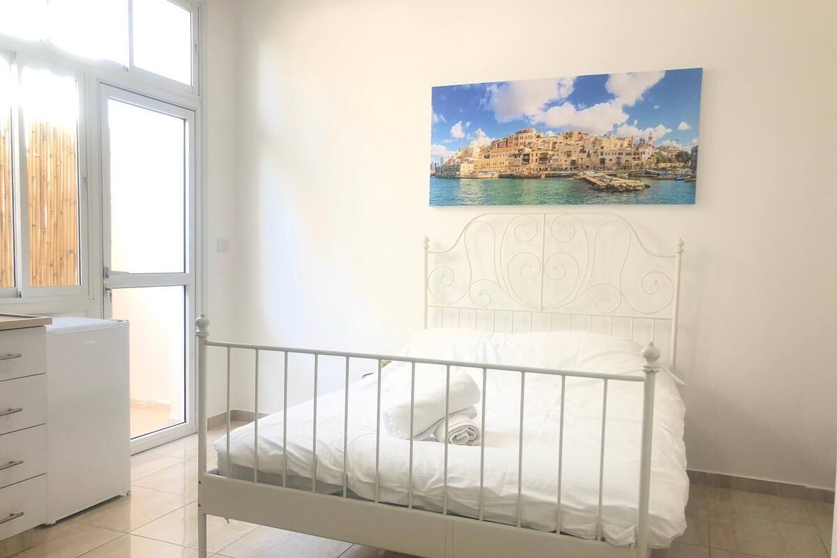A bedroom with a bed, a dresser, and a window with a view of a coastal town.