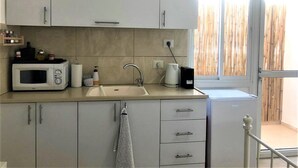 A modern kitchen with white cabinets, a microwave, a sink, and a window with a view of bamboo. - Domos Tiberias (Tiberias)