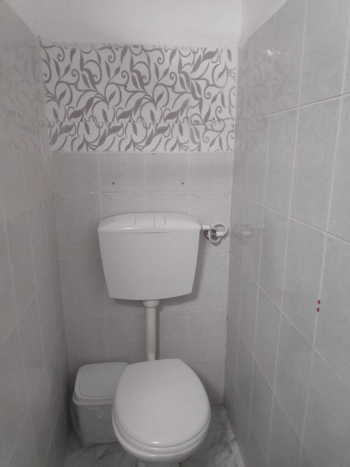 A small, white bathroom with a toilet and a bidet, tiled walls, and a decorative pattern above the toilet.
