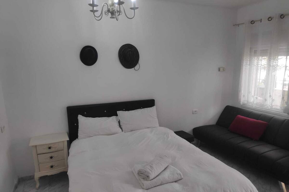 A bedroom with a bed, a nightstand, a dresser, a sofa, and a window with curtains.