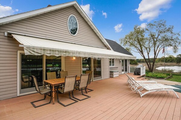 A covered patio with a table and chairs, a grill, and a view of a lake.