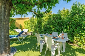 Une terrasse extérieure avec une table et des chaises, entourée de verdure et d’un arbre.