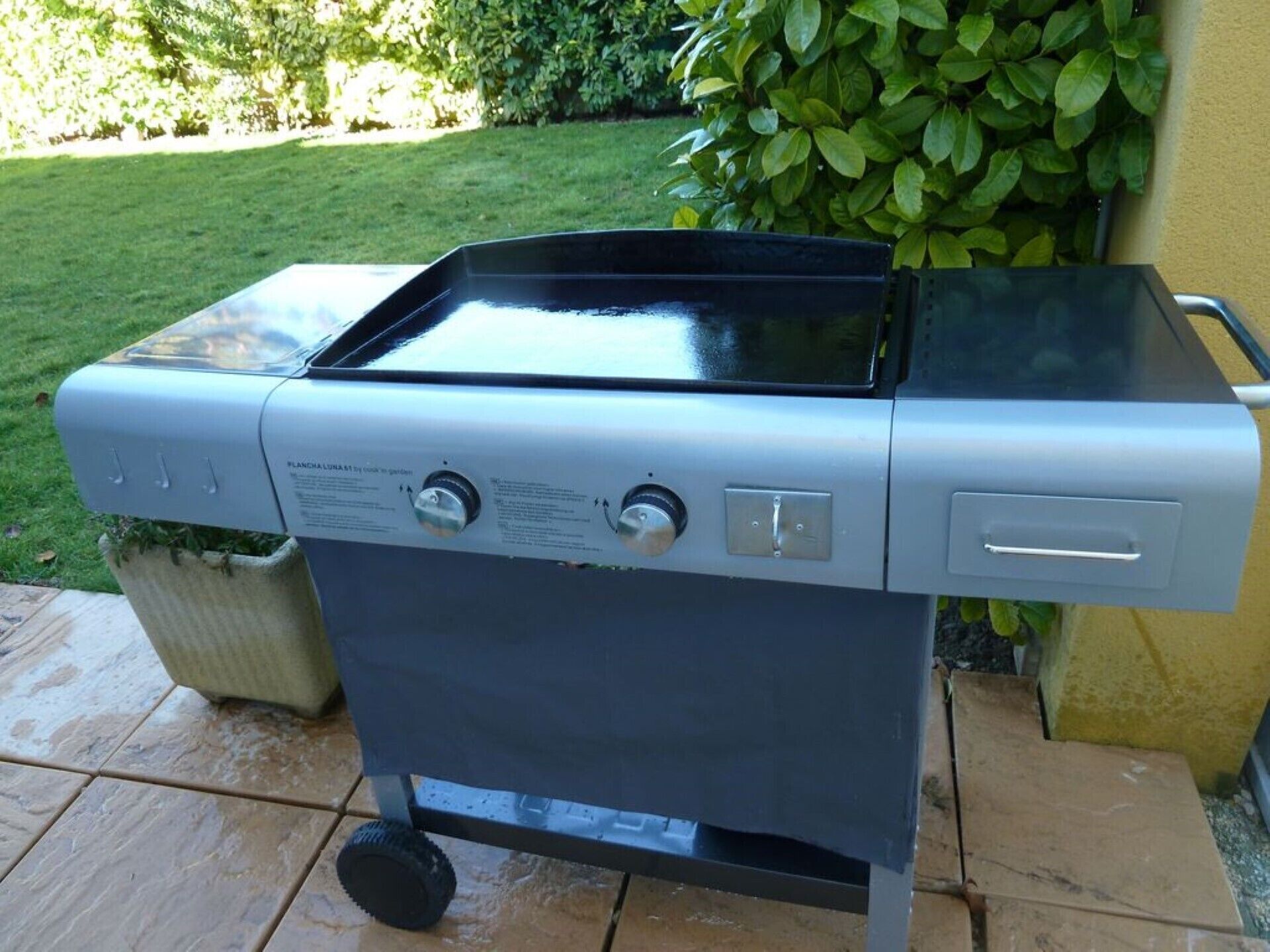Ein tragbarer Grill mit Bedienelementen und Deckel auf einer gefliesten Terrasse.