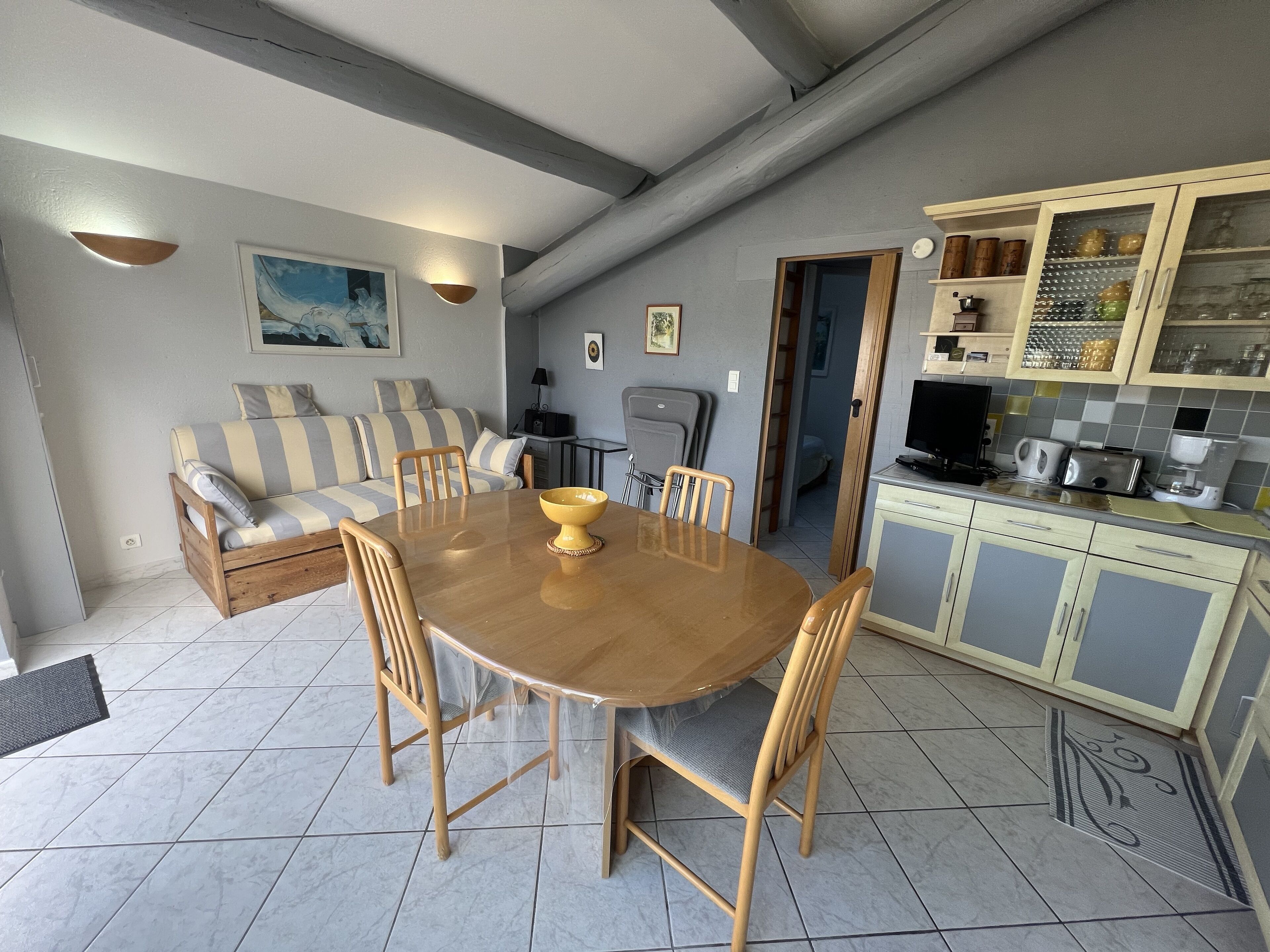 Een ruimtelijk ingerichte leefruimte met een eettafel, stoelen, een bank en een kitchenette.