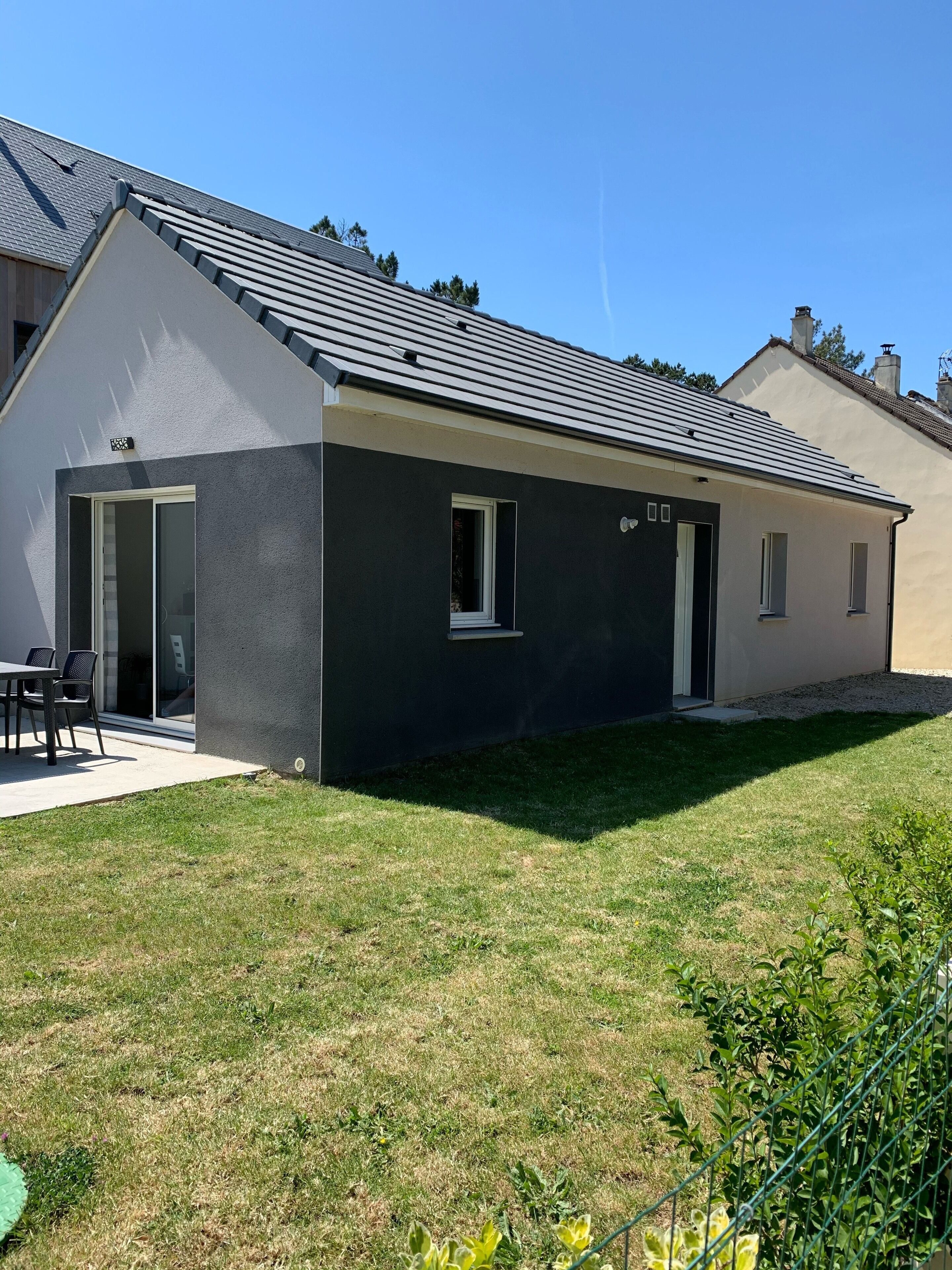 Une maison moderne à deux étages, dotée d’un toit plat, d’un patio couvert et d’une pelouse bien entretenue.