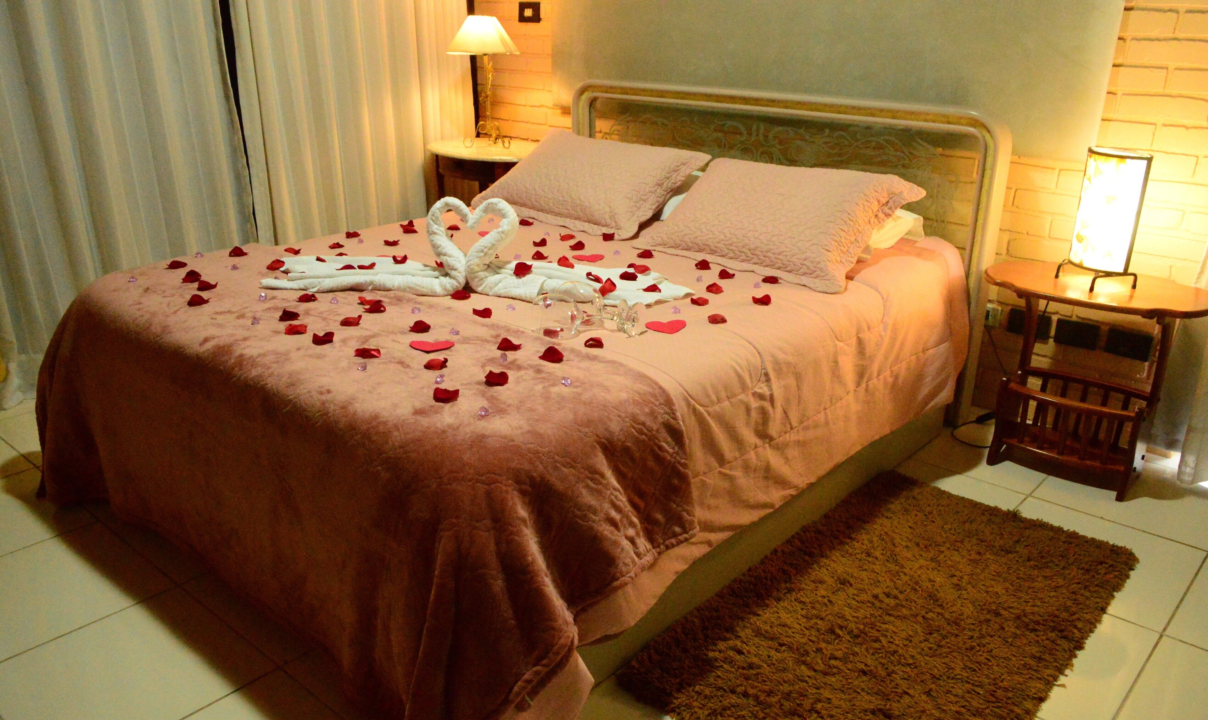 A hotel room with a bed, a nightstand, a lamp, and a small wooden table.