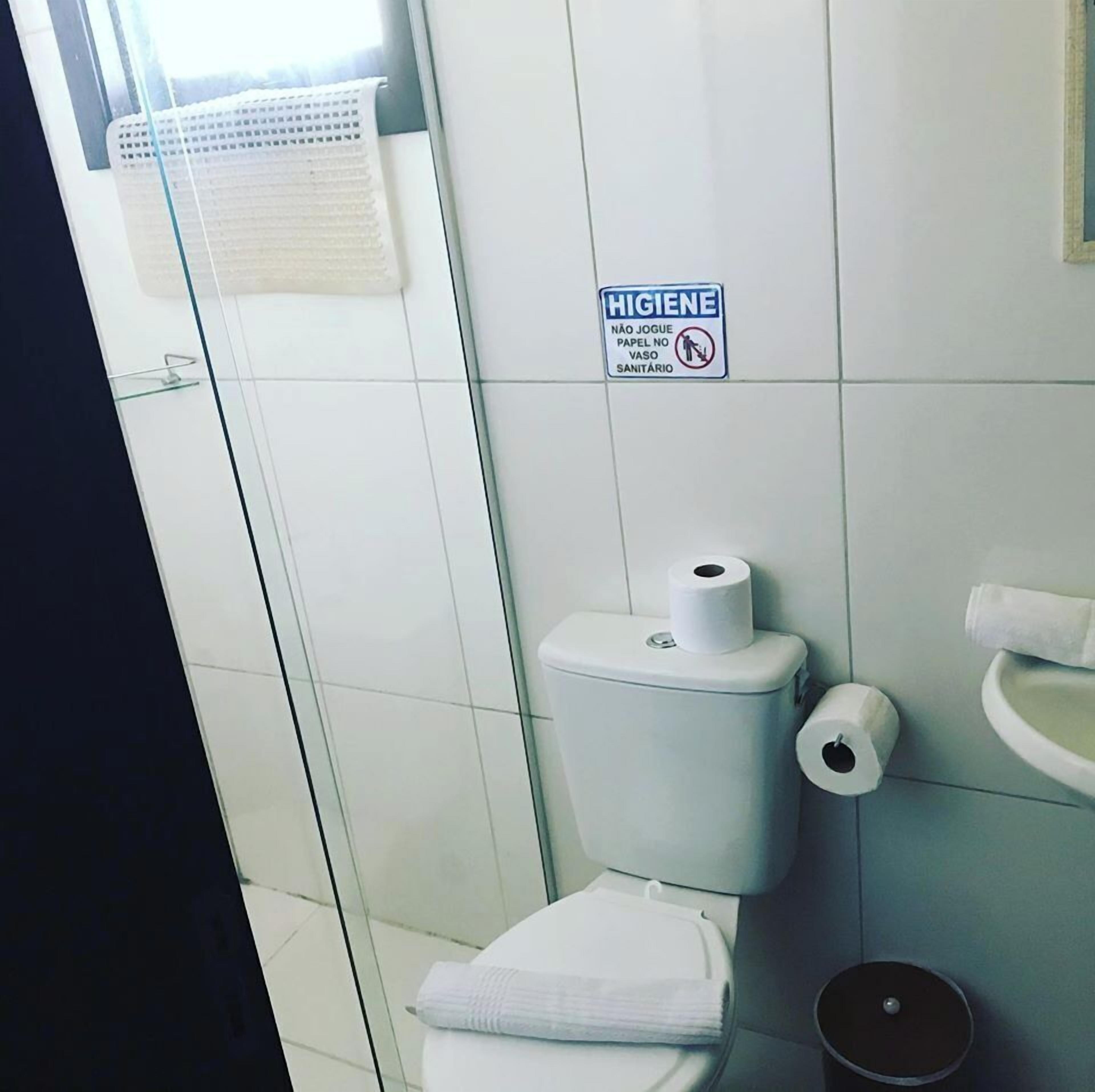 A bathroom with a toilet, a hand dryer, a sink, and a hygiene sign.
