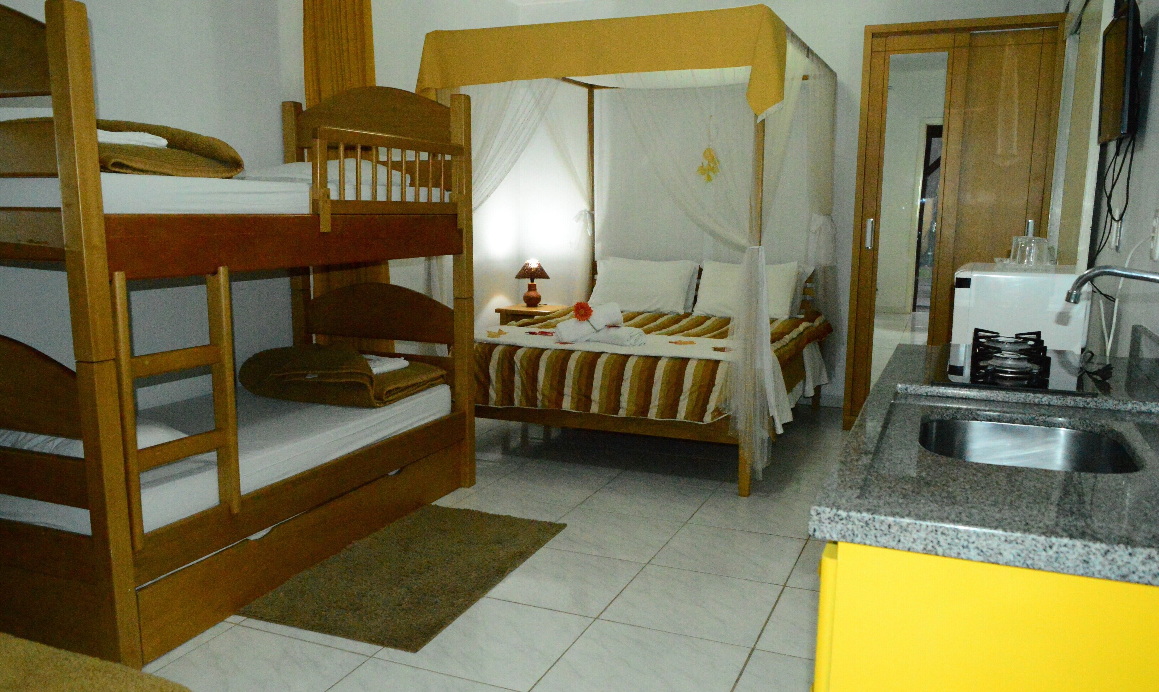 Une petite pièce comprenant un lit superposé, un lit simple avec un baldaquin et une kitchenette équipée d’un évier et d’une cuisinière.