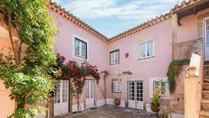 A courtyard with cobblestone flooring, pink buildings, and potted plants. - Casa da Avó Genoveva (Tomar)