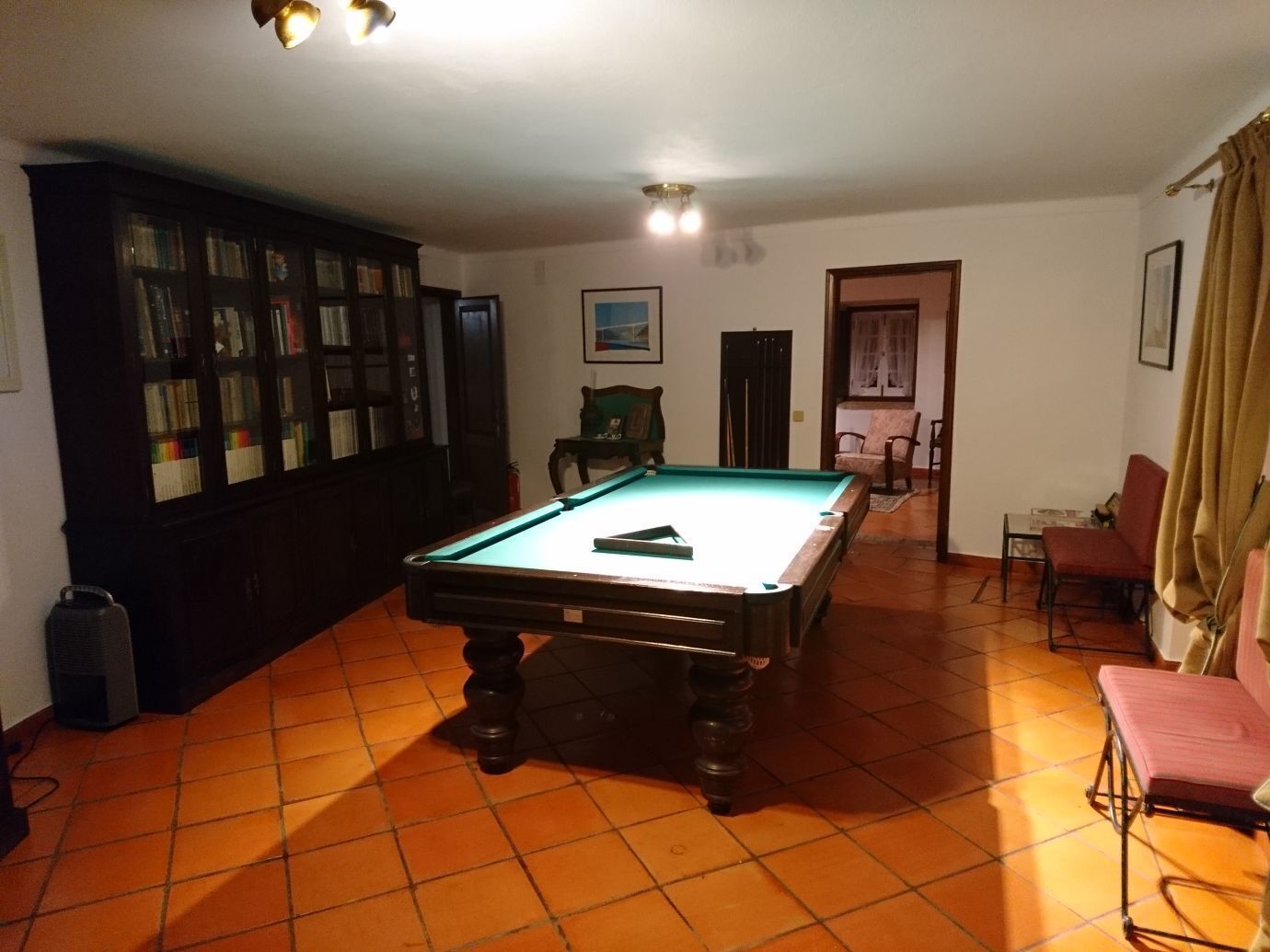 Mesa de bilhar numa sala com soalho em mosaico, estante de livros e porta para outro espaço.
