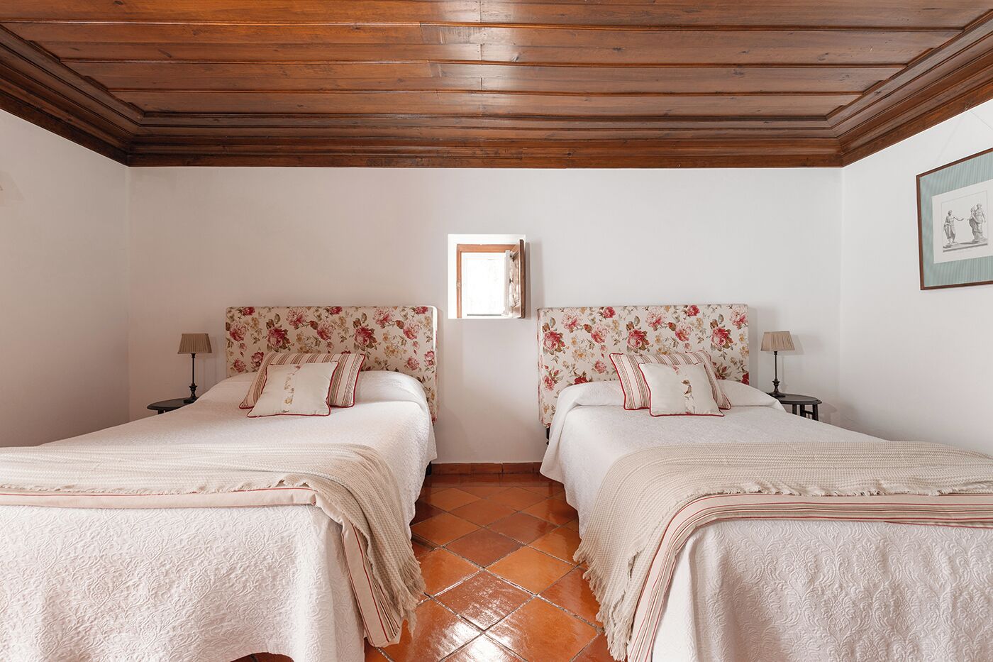 A double room with two beds, wooden ceiling, tiled floor, and a small window.