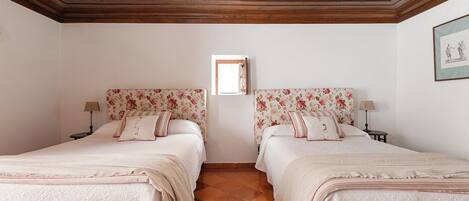 A double room with two beds, wooden ceiling, tiled floor, and a small window.