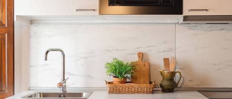 A kitchen with a stainless steel sink, a microwave, and a marble countertop.