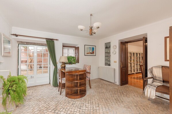 A room with a wooden dining table, a chair, a lamp, a potted plant, a radiator, and a bookshelf.