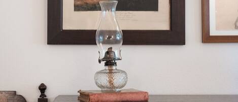 Uma ilustração botânica emoldurada na parede, um vaso de vidro transparente com um objeto decorativo sobre uma mesa de madeira e uma moldura com uma imagem à direita.