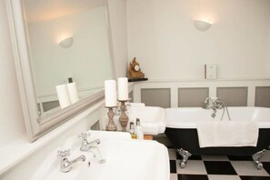 A bathroom with a double sink, a bathtub, a large mirror, and a clock on the wall.
