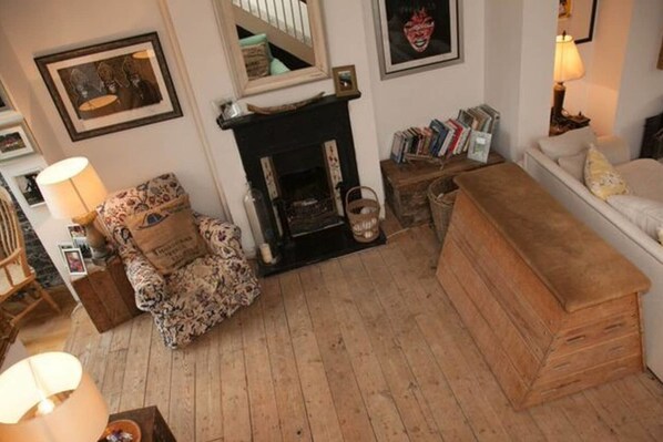 A cozy living room with a fireplace, a sofa, a wooden chest, and a bookshelf.