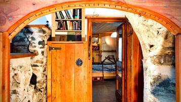 A rustic wooden room with a stone wall, a wooden door, and a bookshelf filled with books.