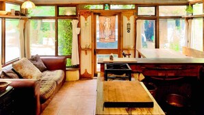 A cozy room with a wooden table, a sofa, and large windows offering a view of greenery outside. - Unique Fairytale Farmhouse Near Galway (Corrandulla)