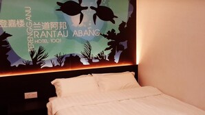 Habitación de hotel con una cama, una pared con un mural de tortuga y un letrero que indica el nombre del hotel y el número de habitación.