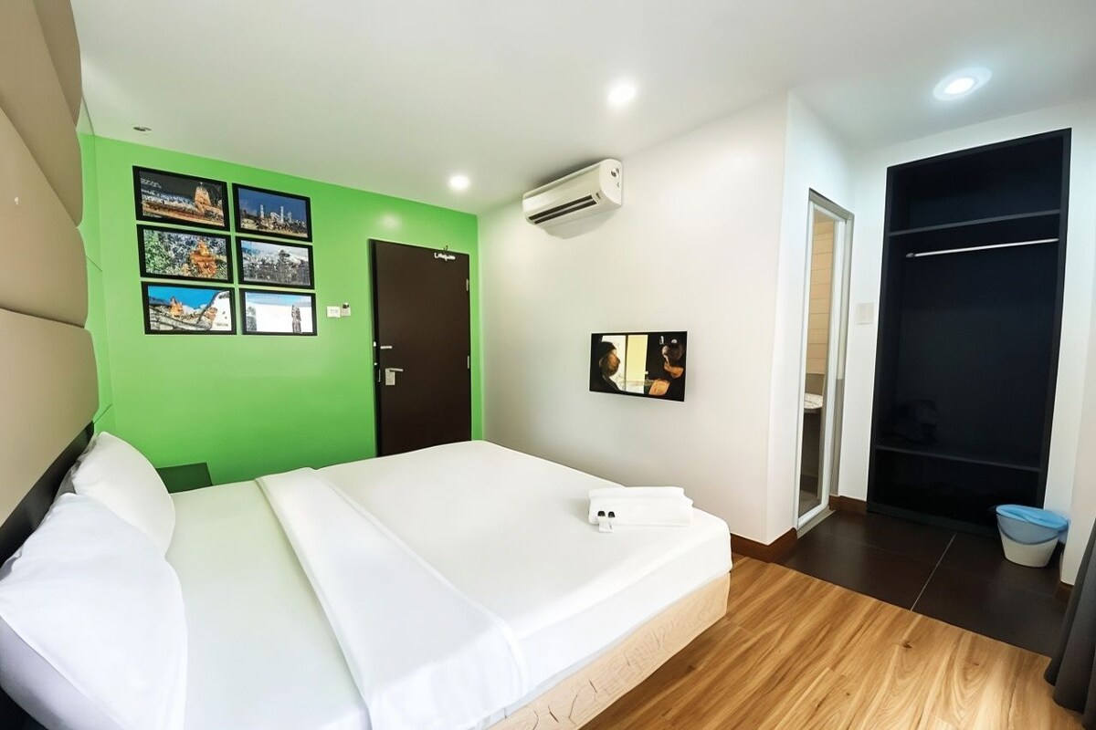 Habitación de hotel con cama, pared de acento verde, televisor de pantalla plana, unidad de aire acondicionado y armario.