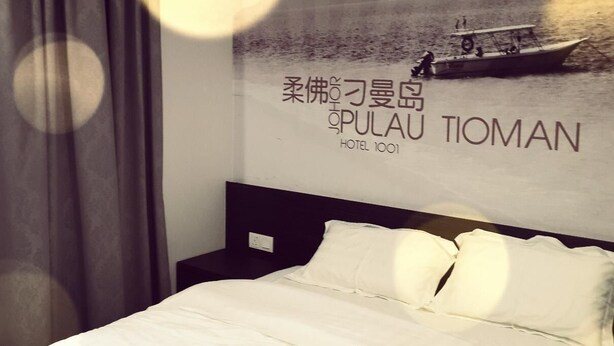 Una habitación de hotel con cama, mesita de noche, una pared con un cartel y una cortina.