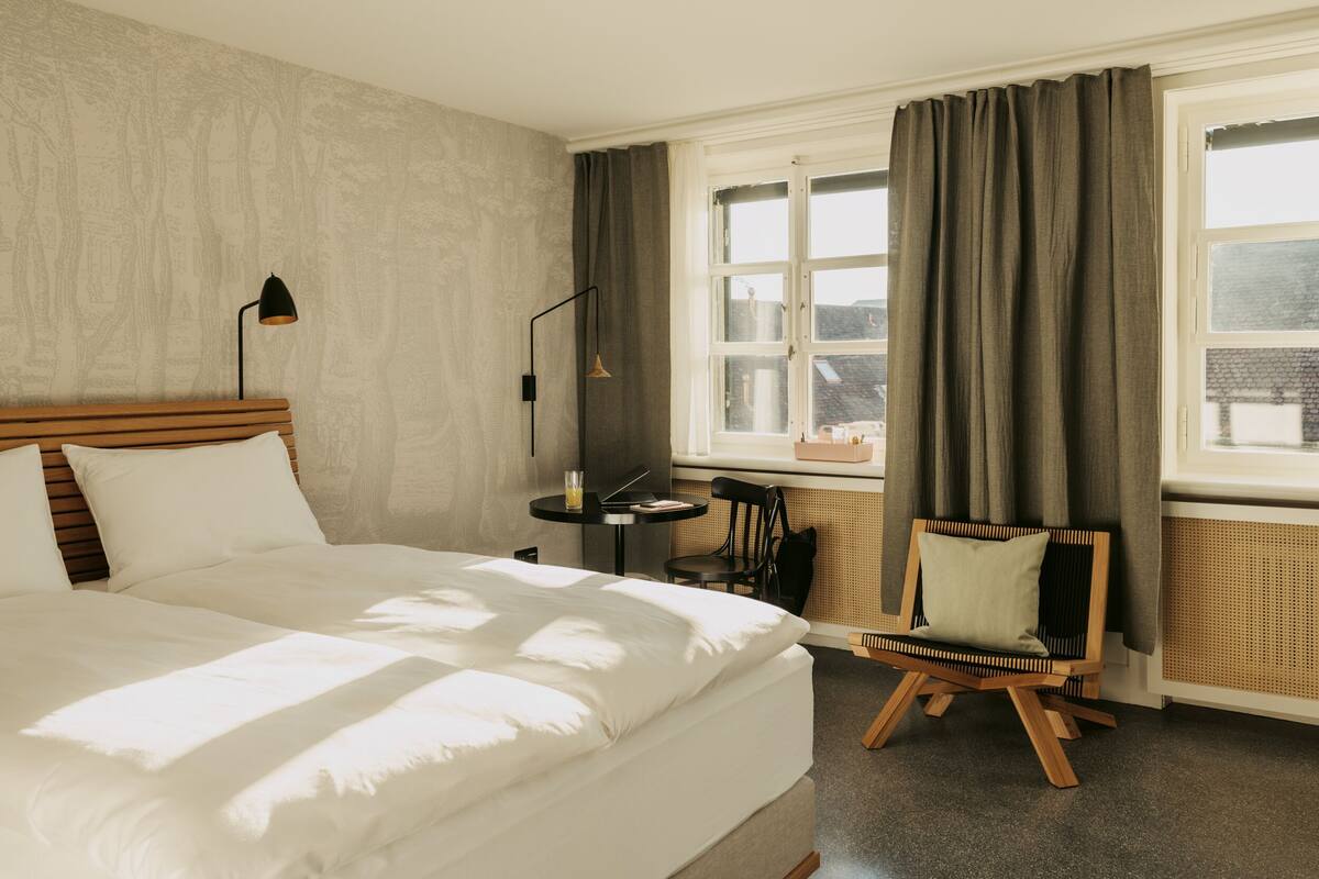Habitación de hotel con una cama grande, un escritorio, una silla y una ventana con cortinas.